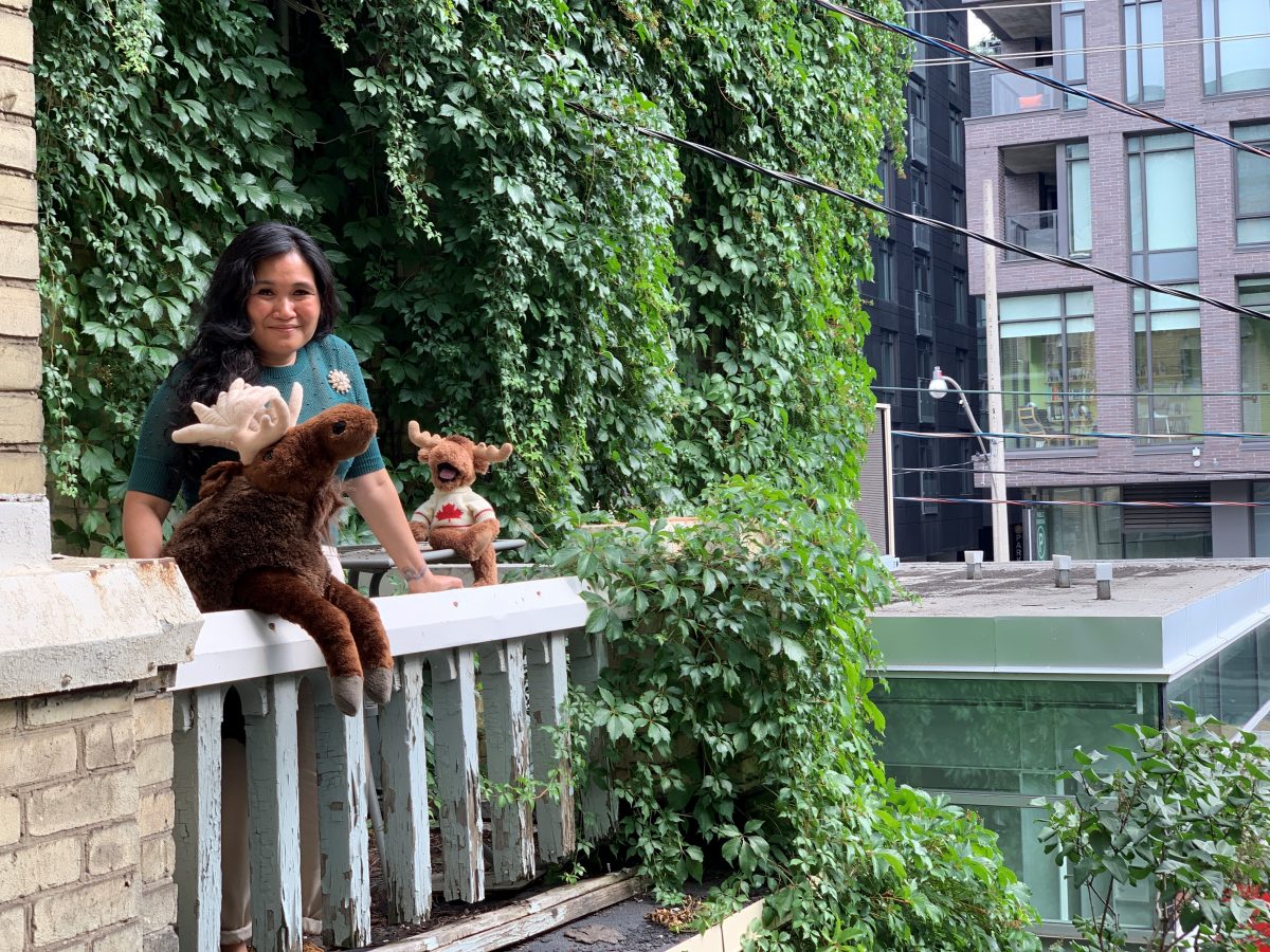 Photo of Artistic Director Nina Lee Aquino on Factory Theatre's balcony. She poses with two plush Mooses.